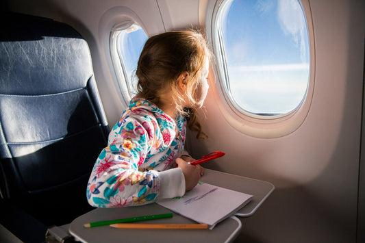 Girl looking out of the plane window while drawing a picture
